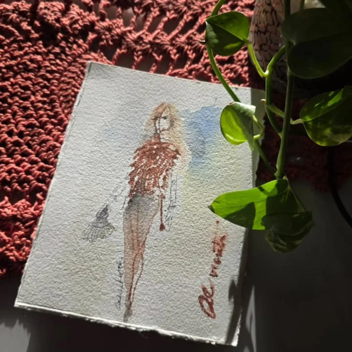 Desenho de moda em aquarela sobre uma mesa com planta e luz solar.